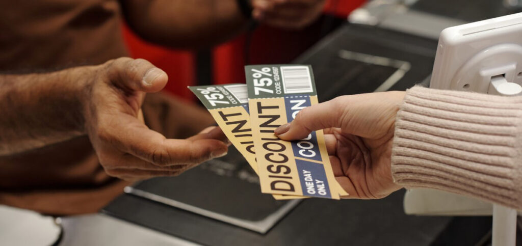 Closeup of a person handing over two discount coupons to a cashier at a grocery check-out line.